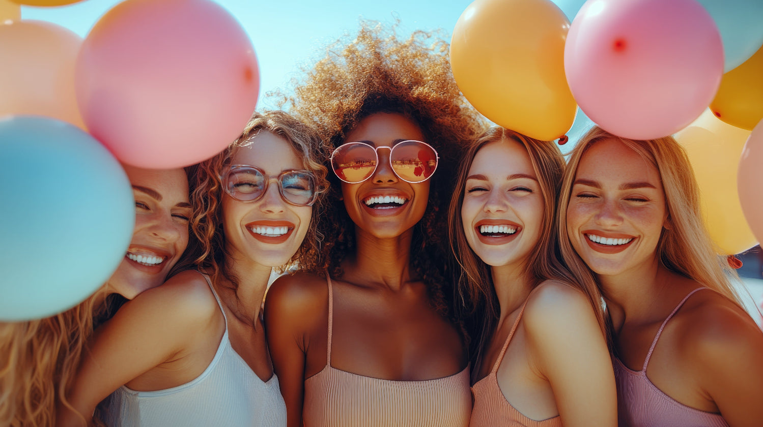 Five women posing together with colorful balloons against a clear blue sky.